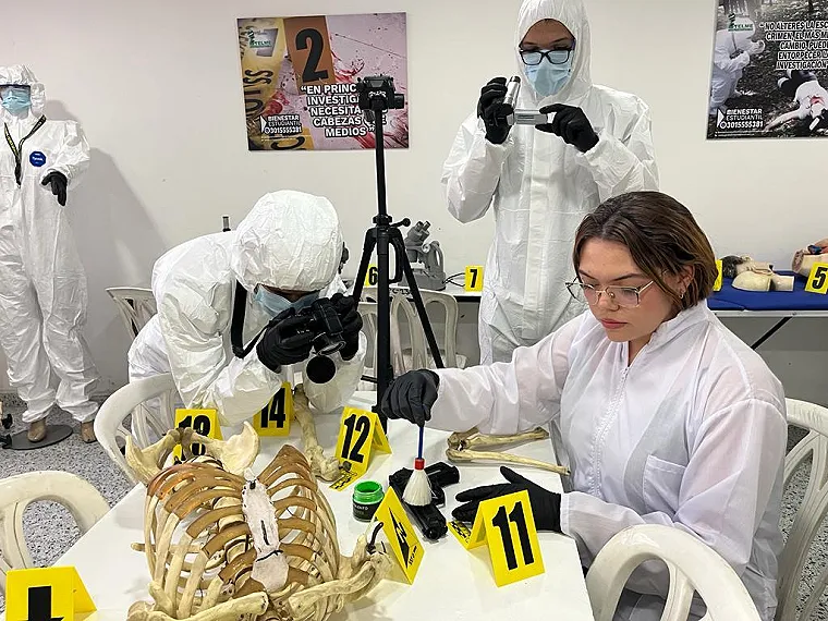 Estudiante con traje de protección fotografía la evidencia mientras su compañera la analiza