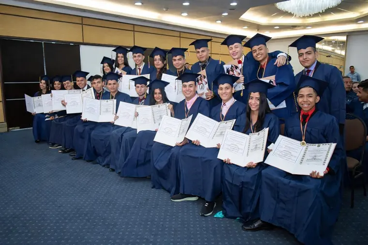 Graduados sentados en un salón mostrando sus diplomas