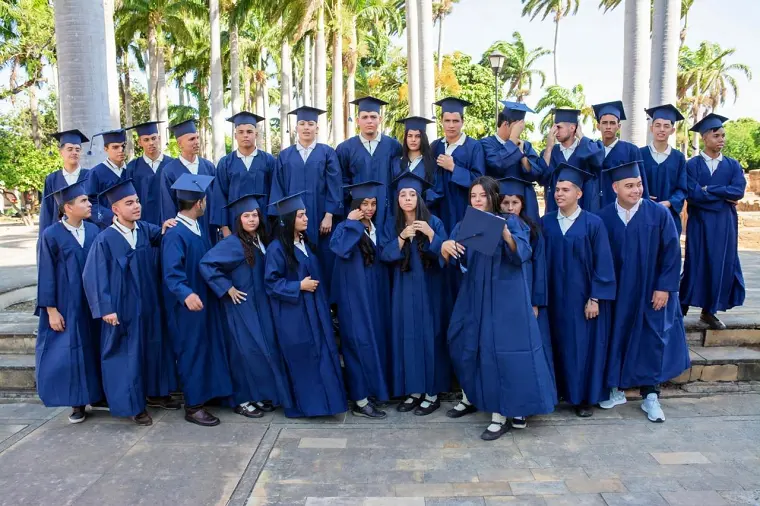 Promoción de graduados con toga y birrete azul posando bajo las palmeras