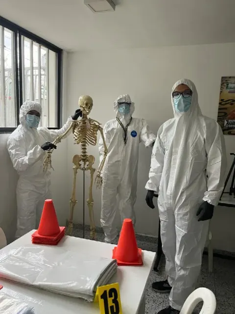 Estudiantes con traje de protección junto a un esqueleto en el laboratorio de criminalística
