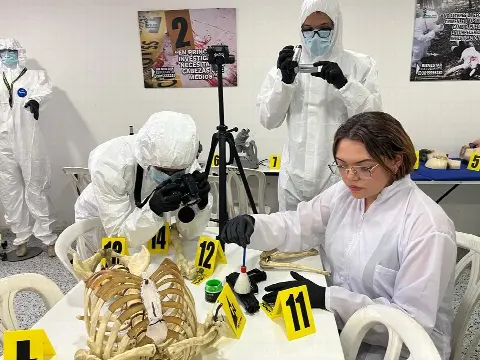 Estudiante con traje de protección fotografía la evidencia mientras su compañera la analiza