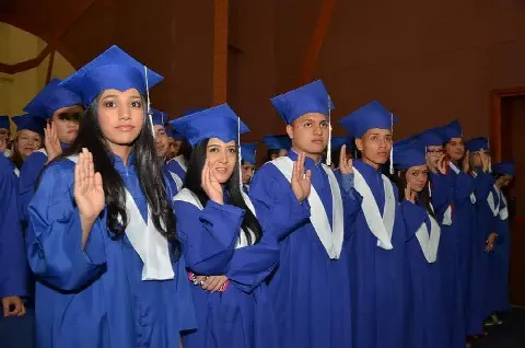 Graduados con toga azul levantando la mano en el juramento