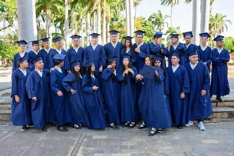 Promoción de graduados con toga y birrete azul posando bajo las palmeras